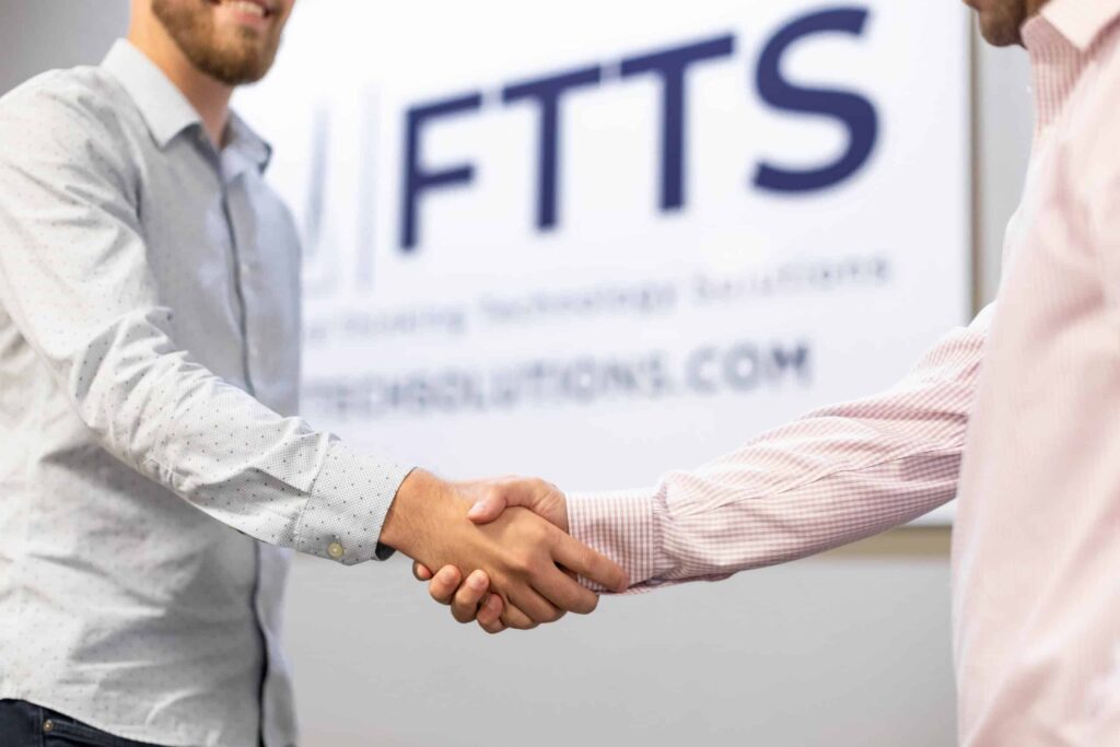 two hands shaking in front of FTTS business sign
